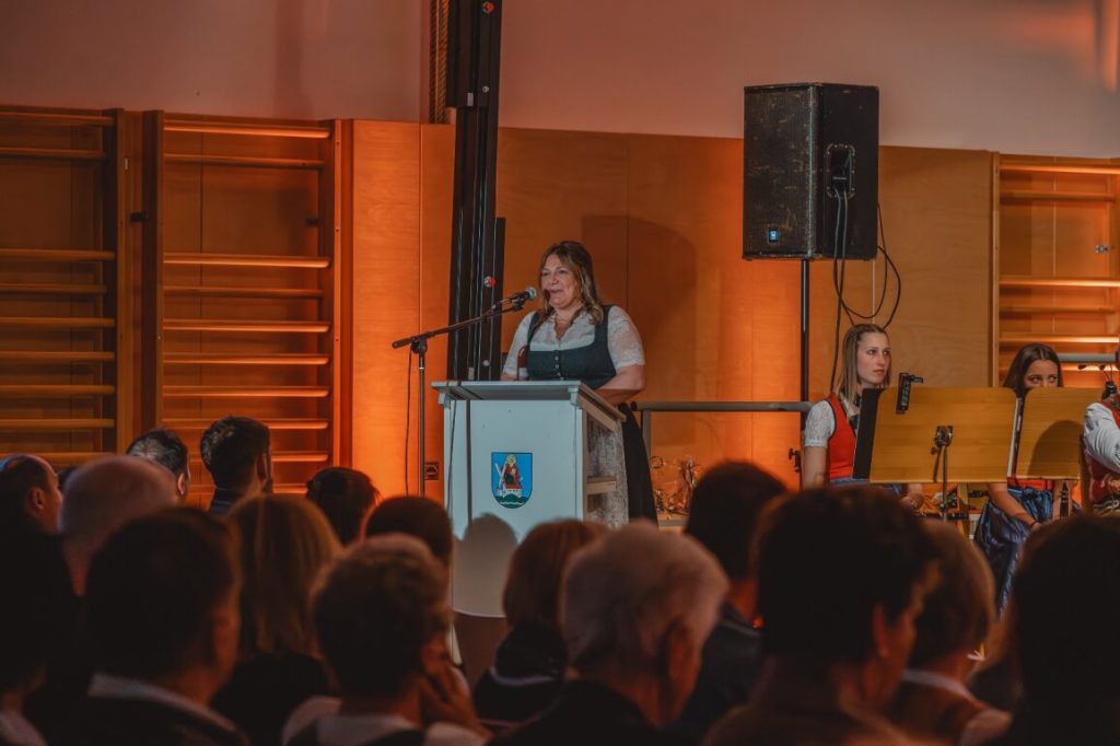 Frau in Tracht spricht bei Veranstaltung der Trachtenmusikkapelle Taxenbach vor Publikum